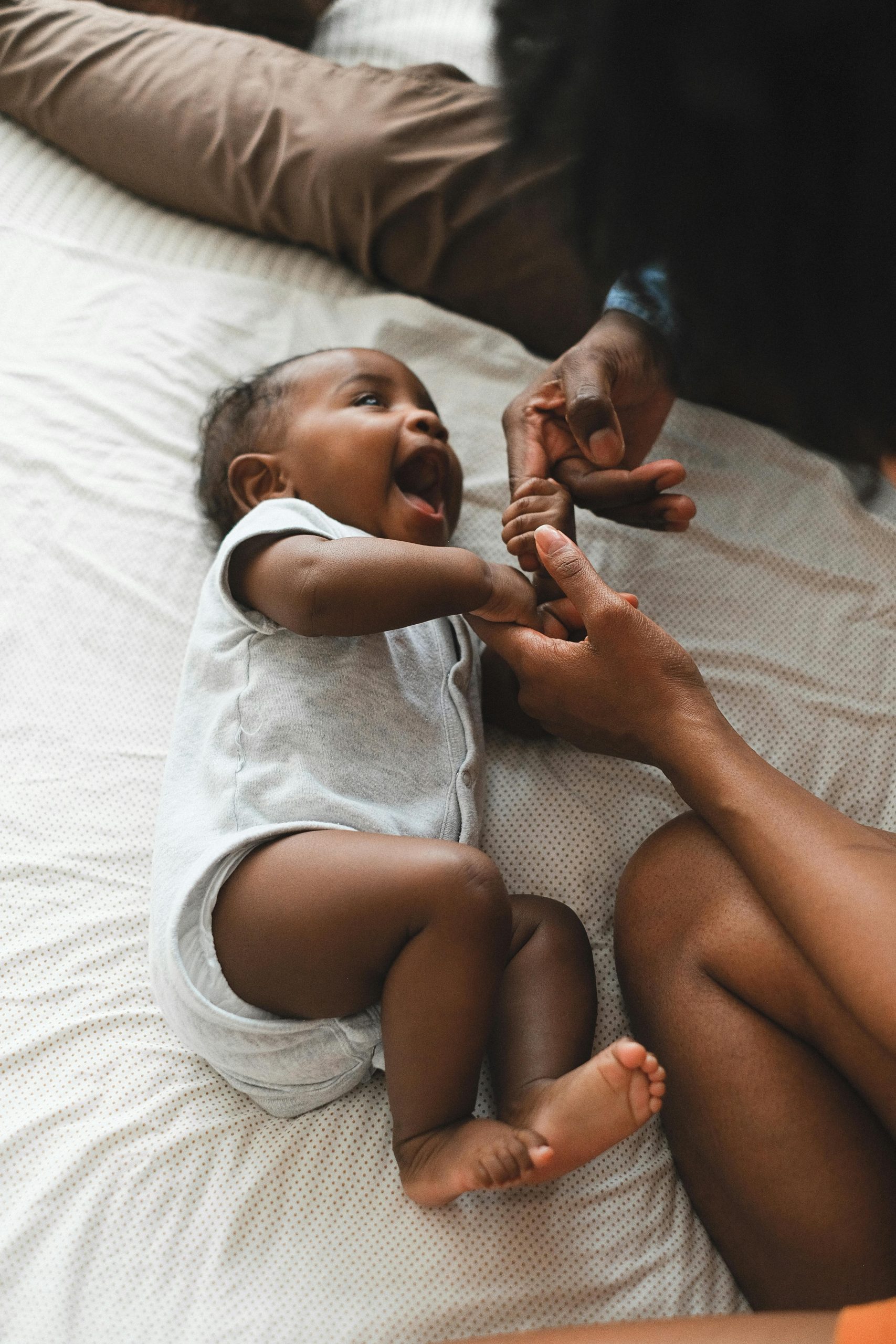 Close-up of a happy baby in a onesie giggling while playing indoors.